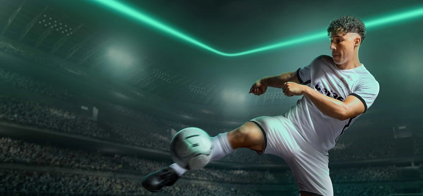 Close-up of a soccer player wearing a shirt with the Bet365 logo volleying a football against a green flood-lit backdrop.