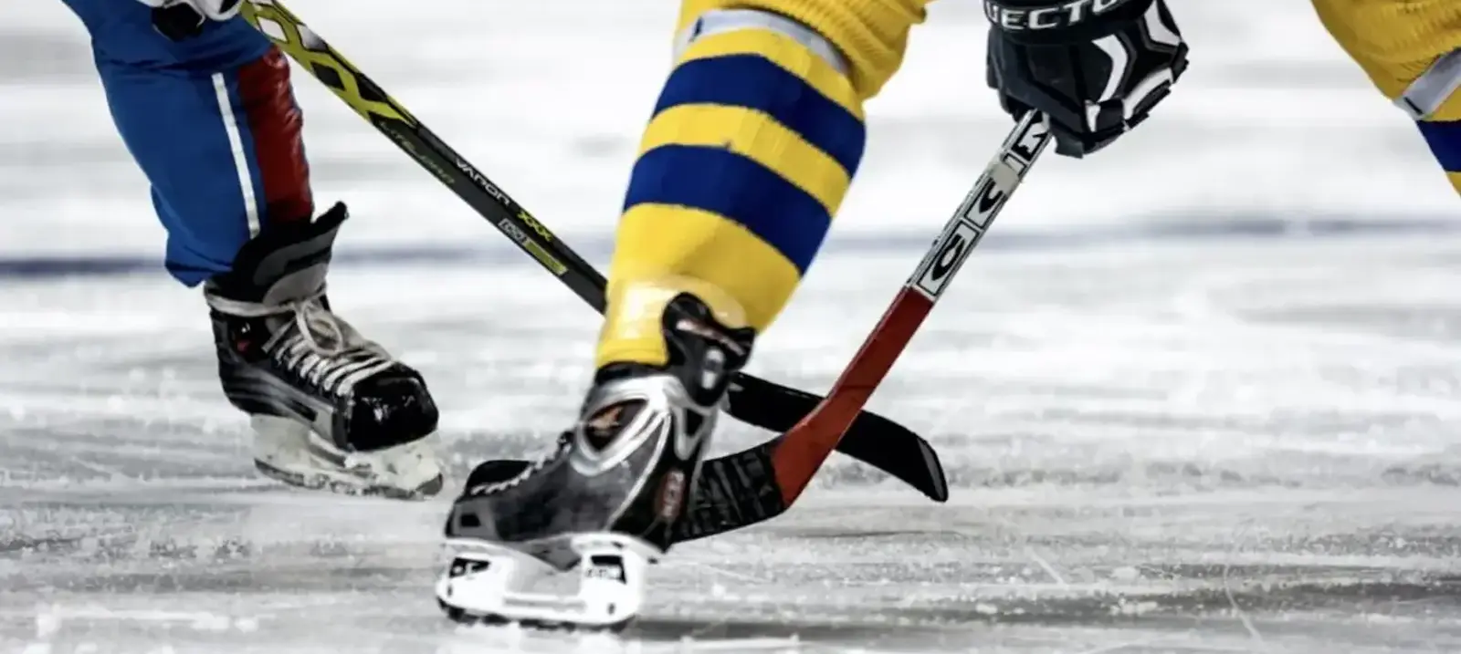 Close-up shot of the boots and sticks of two ice hockey players battling for the puck.