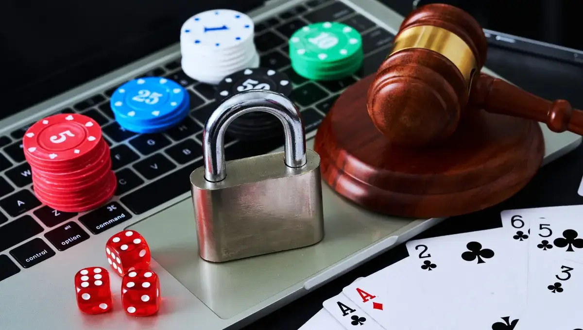 An open laptop with items spread out on the keyboard: a padlock, a judge's gavel, casino chips and dice.